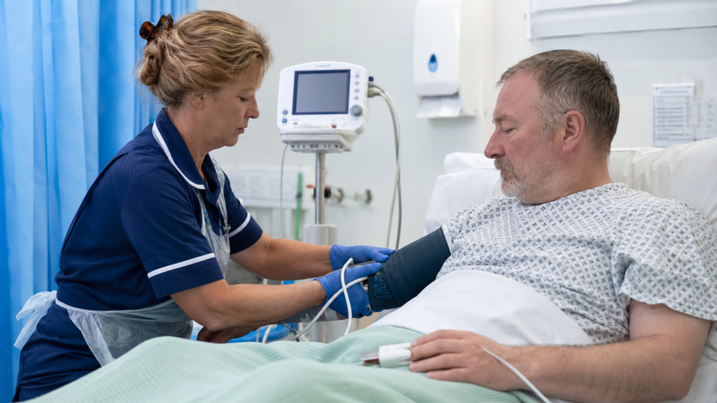 Healthcare support worker checking an adult patient for early signs of deterioration.